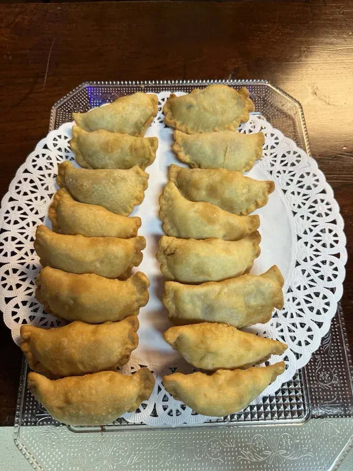 Empanadas doradas dispuestas en dos filas sobre un tapete de papel decorativo, servidas en un plato transparente.