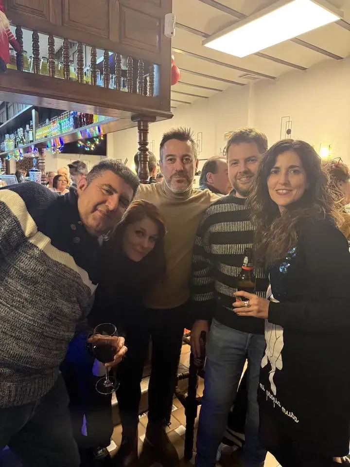 Grupo de personas sonriendo, posando para una foto en un interior, probablemente un pub, con bebidas visibles.