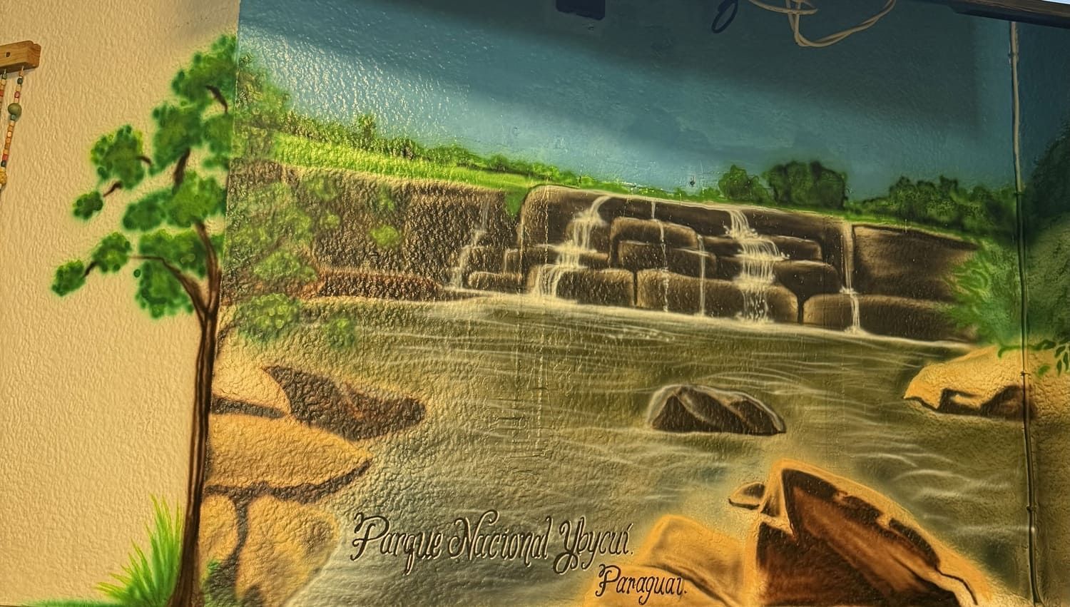 Mural de una cascada de piedra que desemboca en un estanque, bordeado de plantas verdes y rocas.