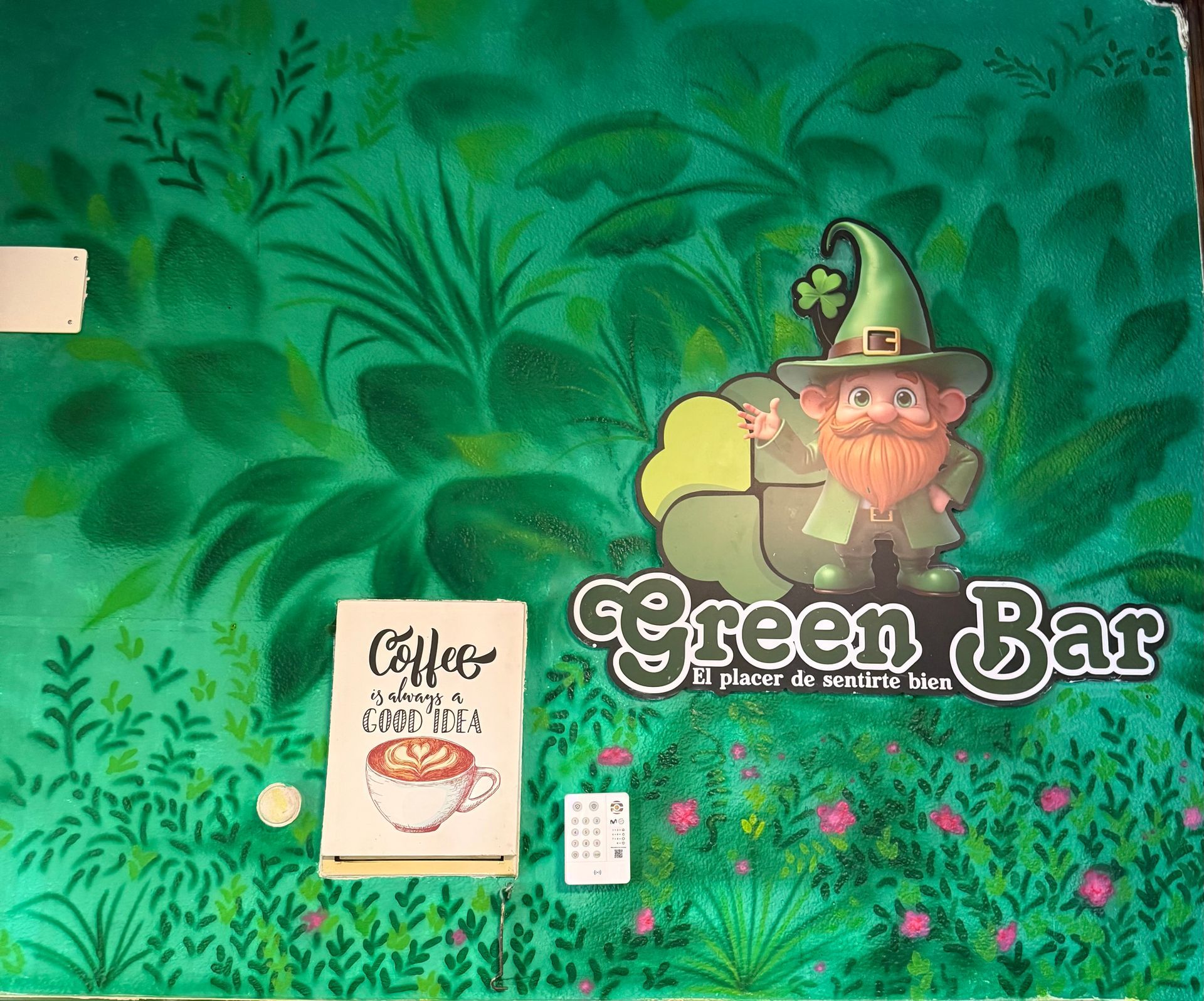 Cartel de Green Bar con un duende sonriente de dibujos animados, tréboles y un gráfico de una pequeña taza de café sobre un fondo verde frondoso.