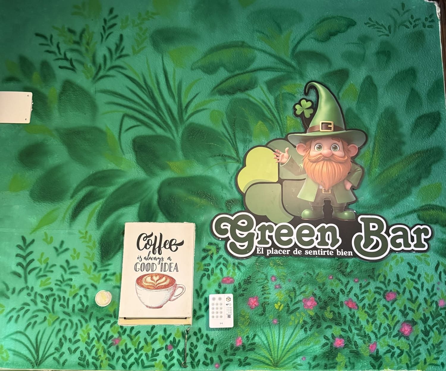 Mural del Green Bar con un duende de dibujos animados, hojas verdes exuberantes y el dibujo de una taza de café.