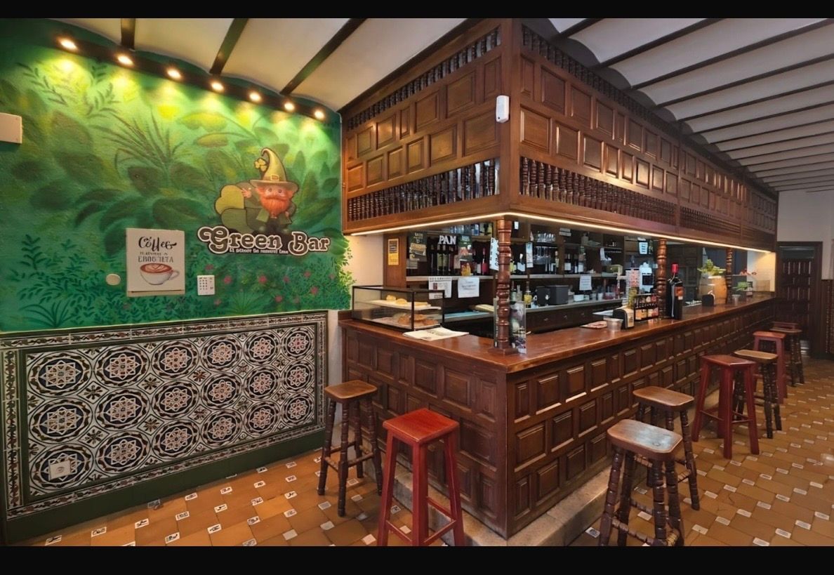 Acogedor bar con paneles de madera y taburetes, suelo de baldosas y decoración mural iluminada con motivos vegetales.