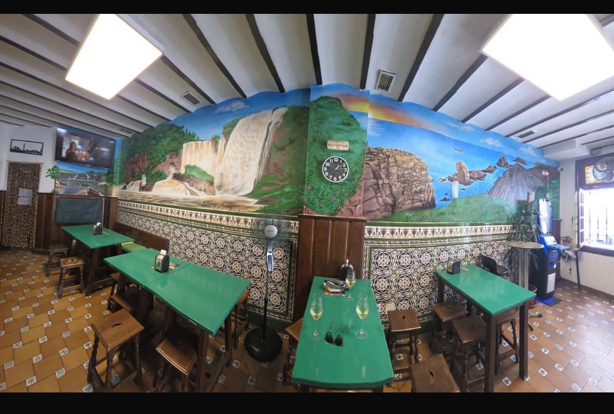 Interior de restaurante rústico y colorido con mesas verdes, paredes de mosaico y decoración mural paisajística.