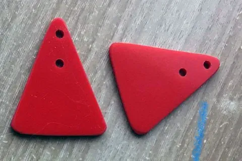 Dos triángulos rojos con agujeros están sobre una superficie de madera.