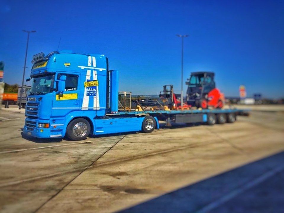 Lkw in einem Parkbereich mit Baumaschine als Ladung