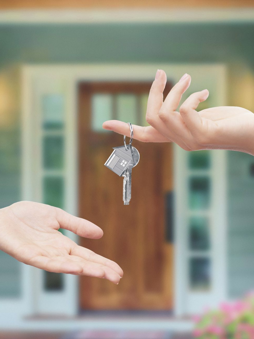 Main passant les clés de la maison devant la porte d'entrée d'une maison