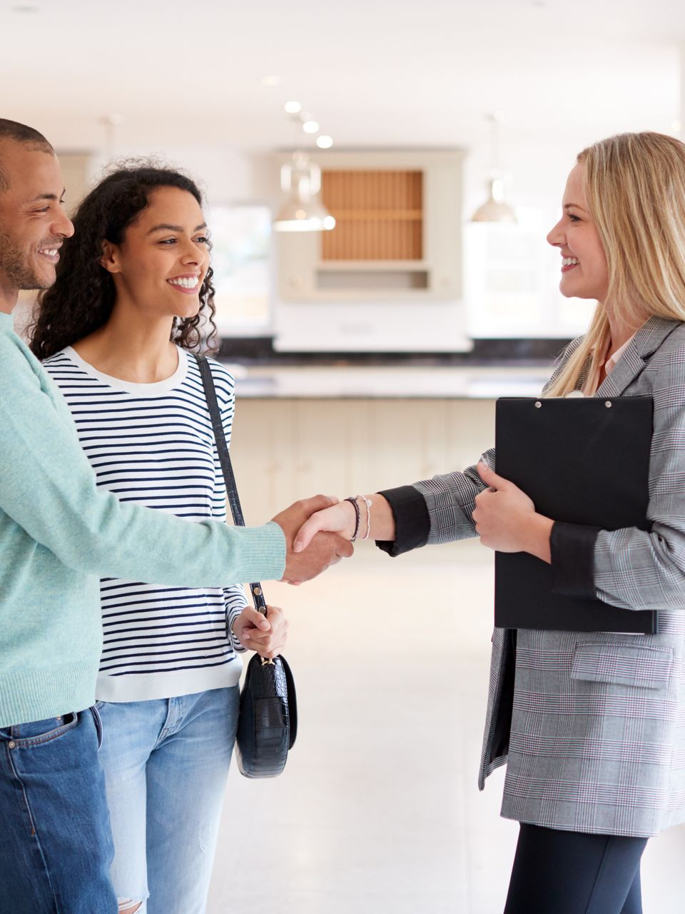 Un agent immobilier serre la main d'un couple dans la cuisine d'une maison