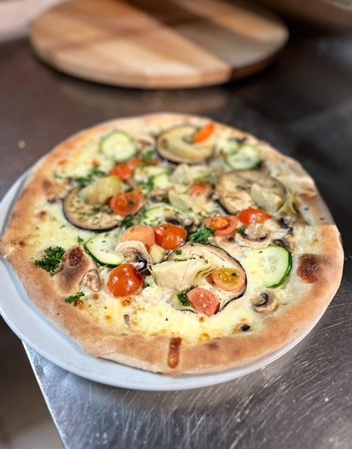 Une pizza avec des légumes dessus est sur une assiette sur une table.