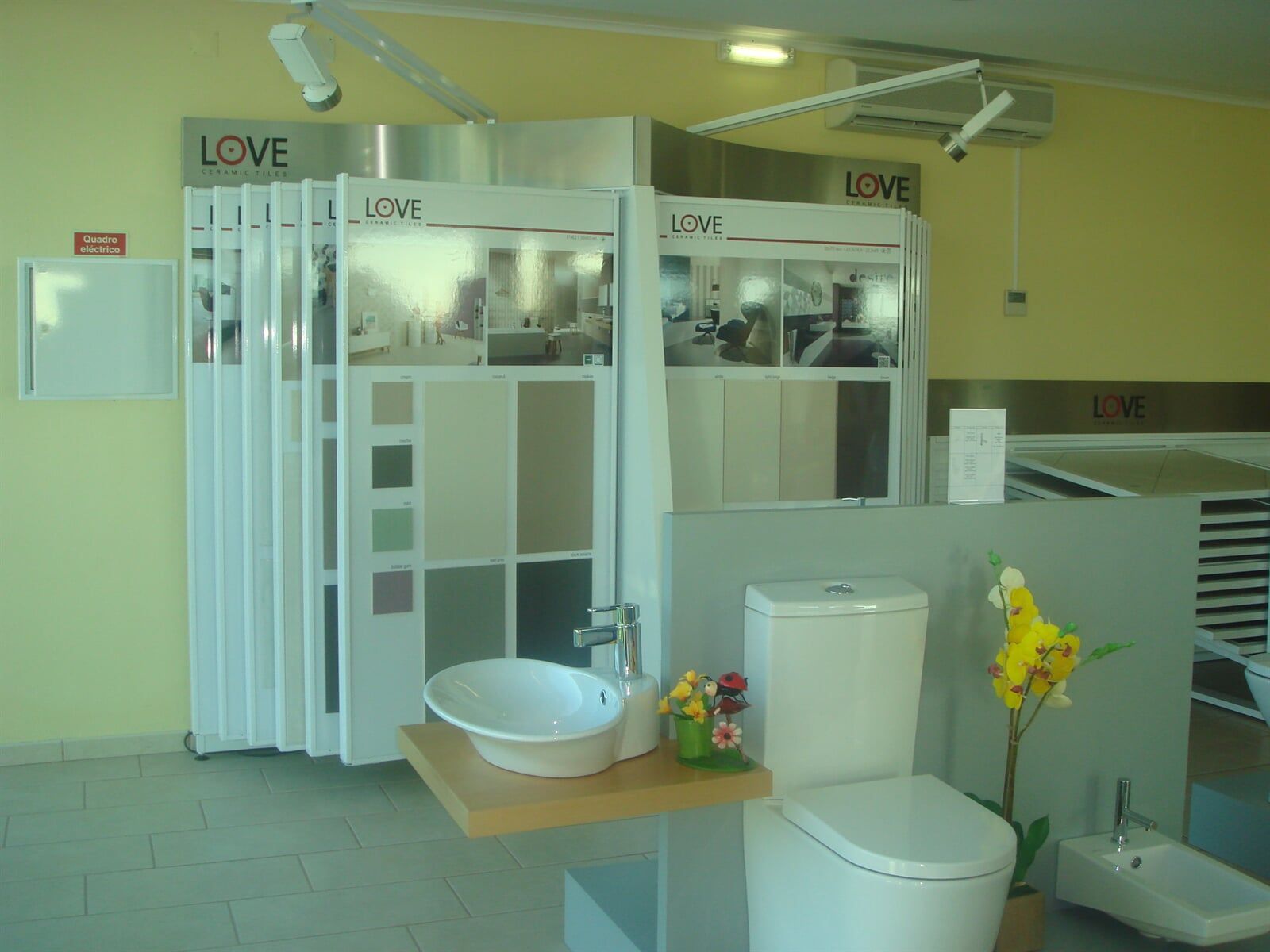 Vitrine de loja de banheiro com amostras de azulejos, vaso sanitário, pia e flores.