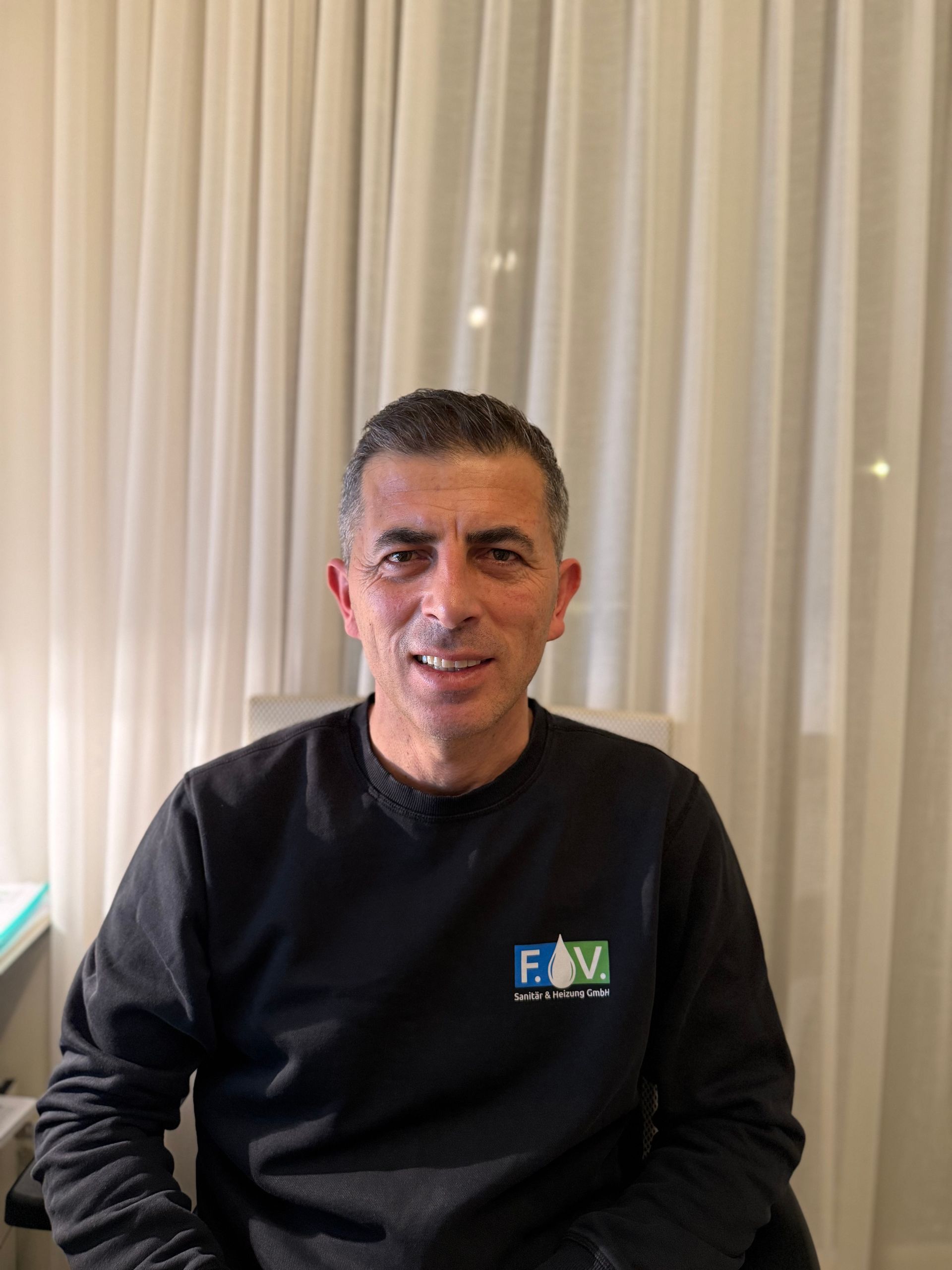 Ein Mann repariert in einem Innenraum einen Warmwasserbereiter, indem er mit Werkzeugen ein Rohr verbindet.