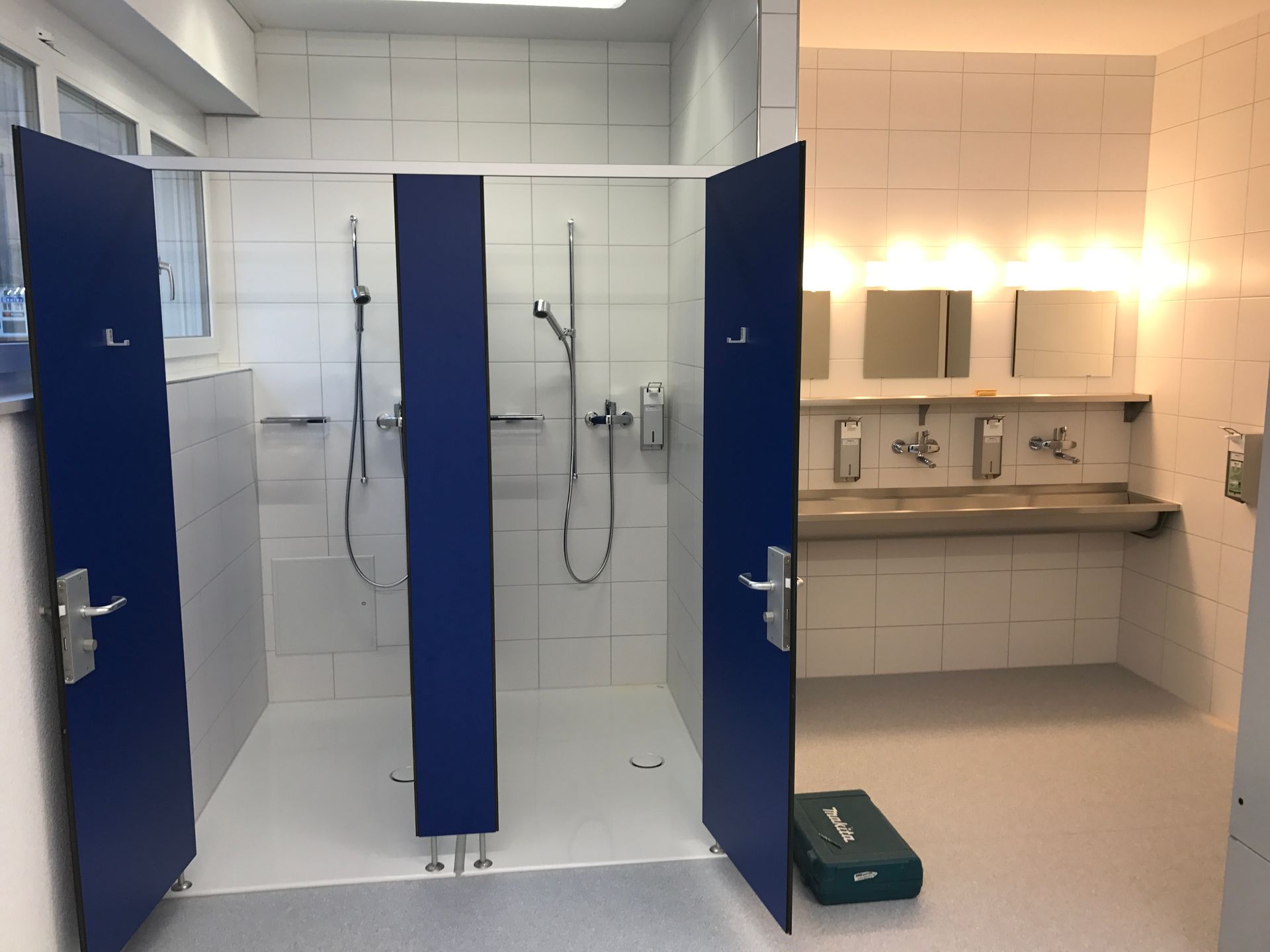 Klempner benutzt Schraubenschlüssel unter einem weissen Waschbecken im Badezimmer. Blauer Overall, Werkzeug auf dem Boden.