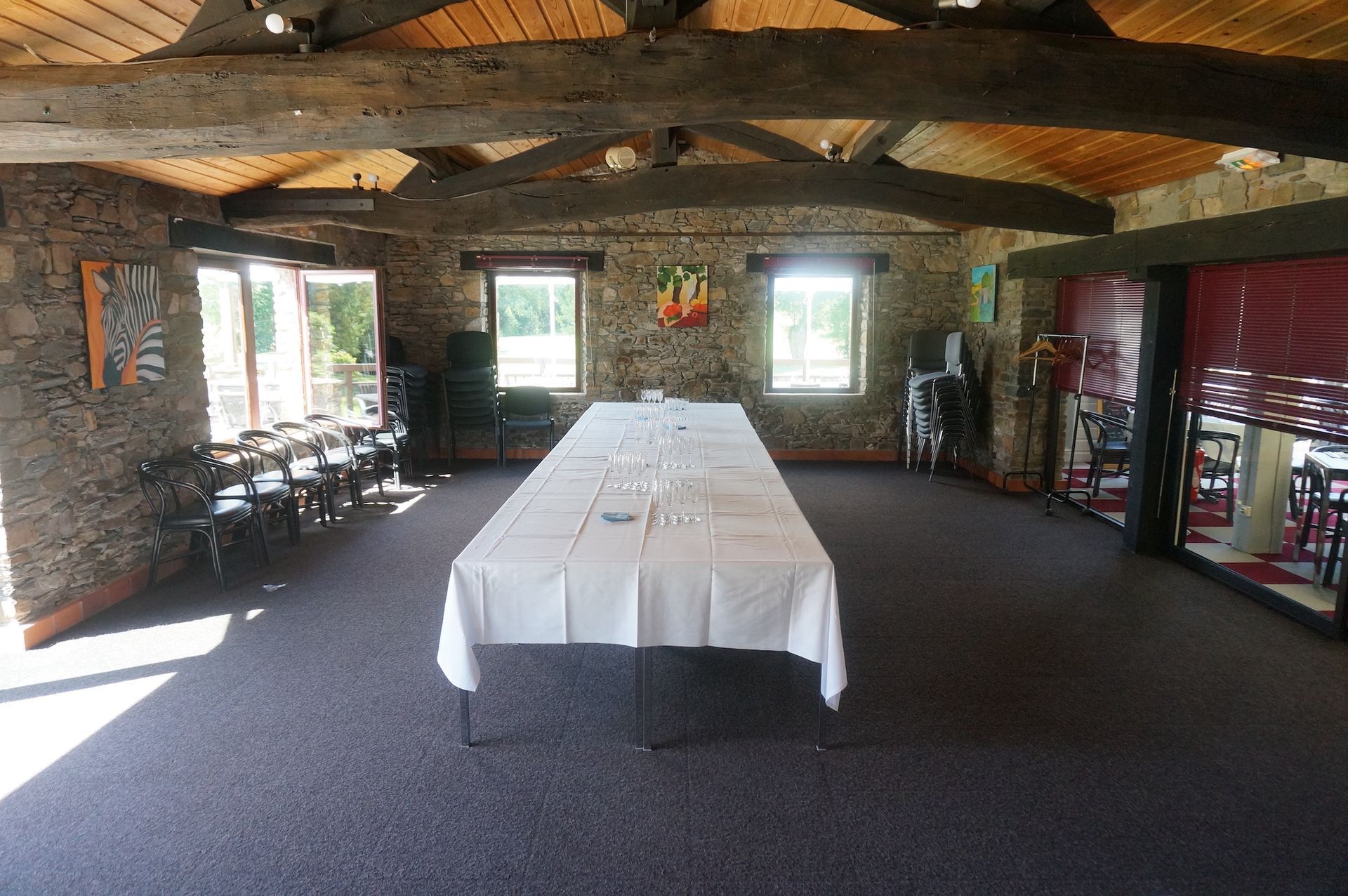 Grande pièce rustique avec murs en pierre, poutres apparentes et une longue table recouverte d'une nappe blanche au centre.