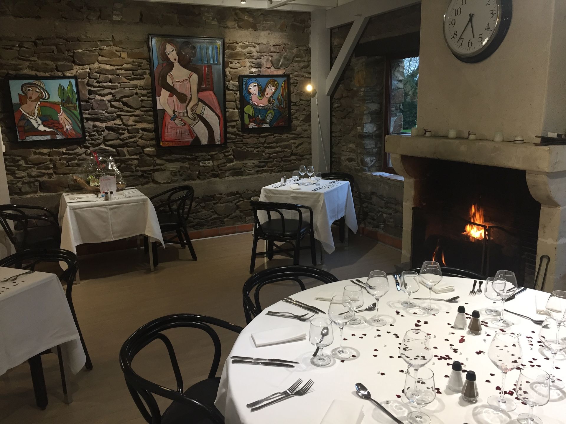 Salle à manger chaleureuse d'un restaurant avec nappes blanches, décorations murales et cheminée allumée.