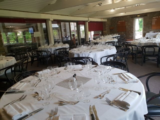Salle à manger dressée avec des tables rondes nappées de lin blanc et des chaises noires, prête pour un événement