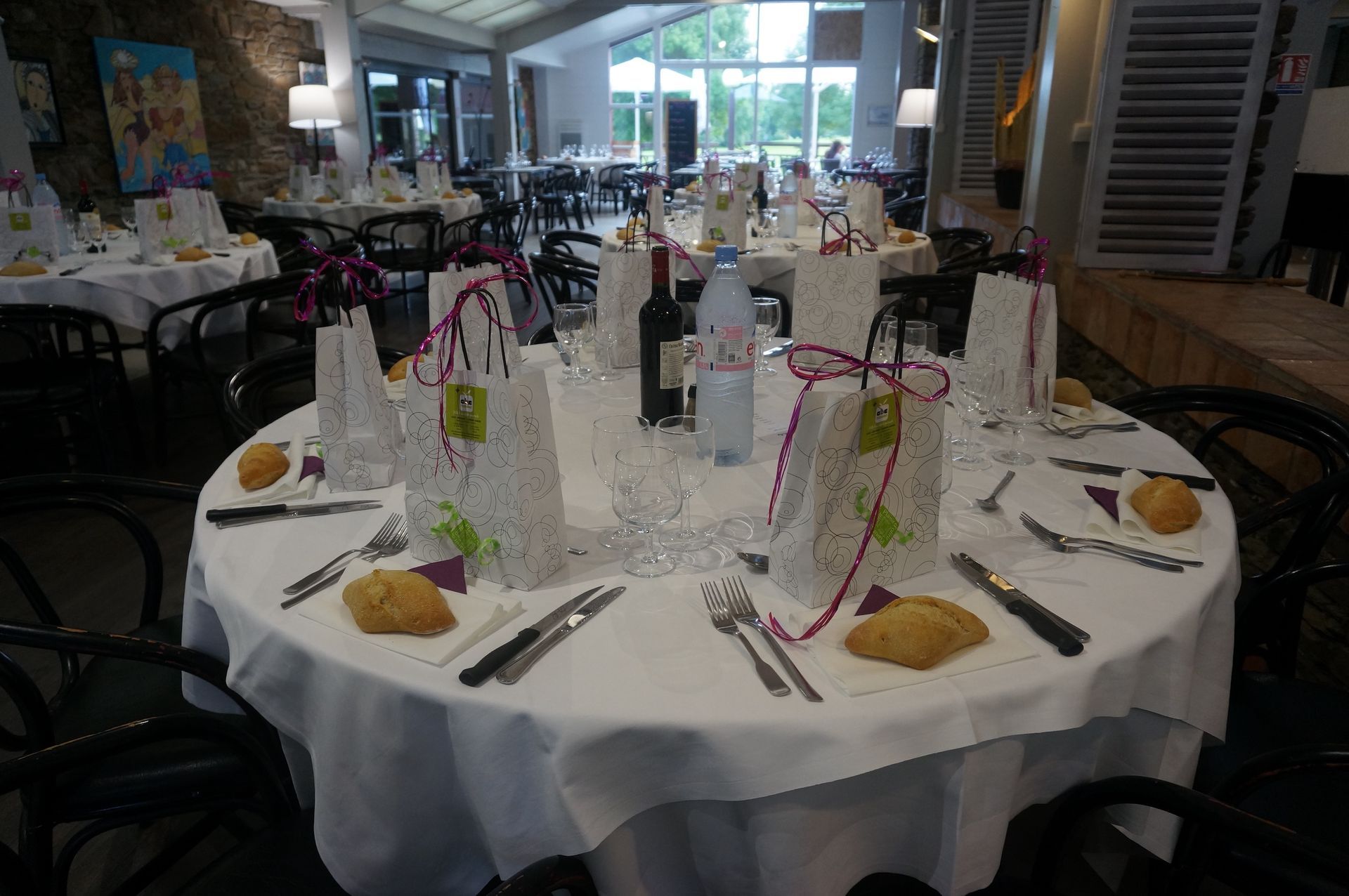 Table ronde dressée pour un banquet, avec nappe blanche, bouteilles en verre, assiettes et serviettes, dans une salle à manger de restaurant.