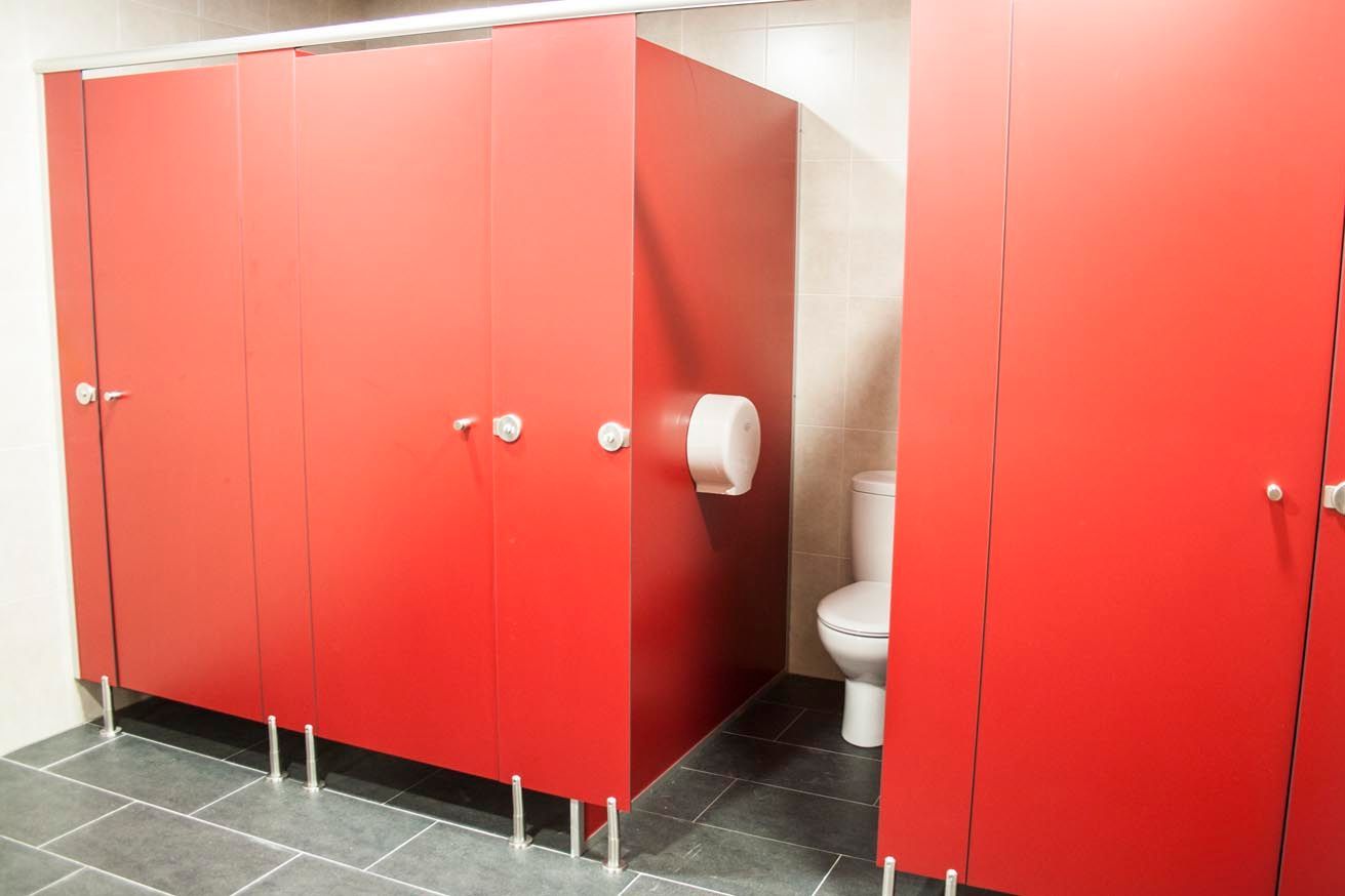 Cabinas de baño rojas en un baño público. Se ven un inodoro blanco y un dispensador de papel higiénico.