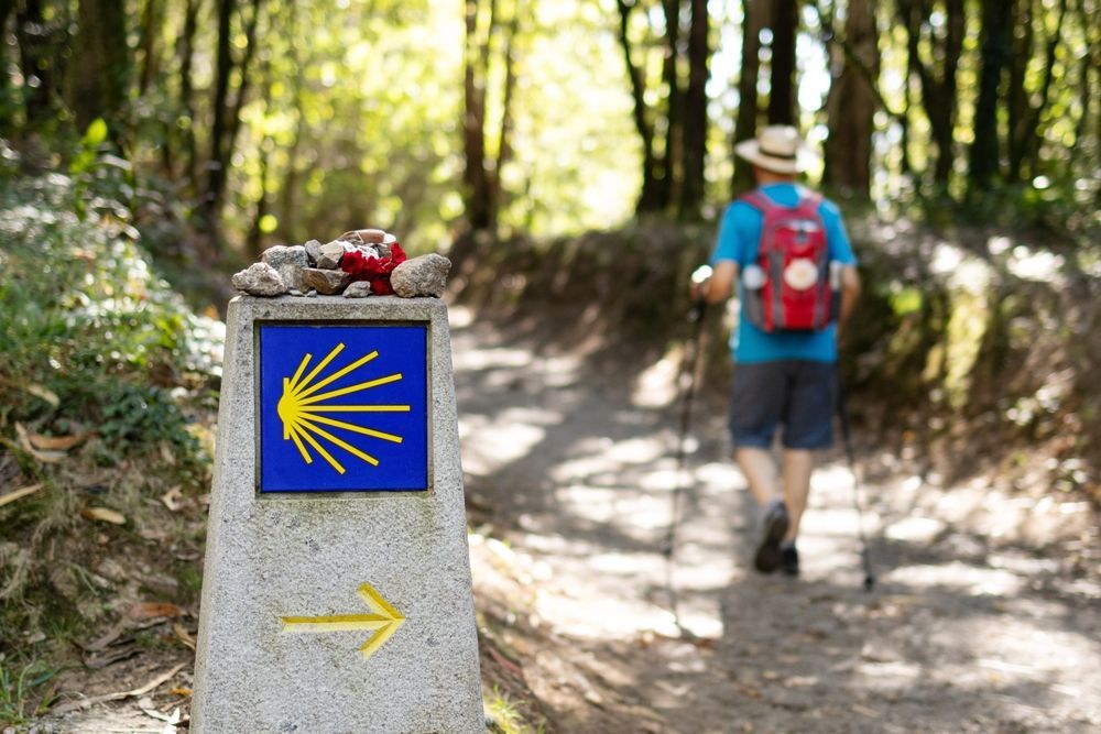 El peregrino recorre el Camino de Santiago, marcado por una señal azul con una concha de vieira amarilla.