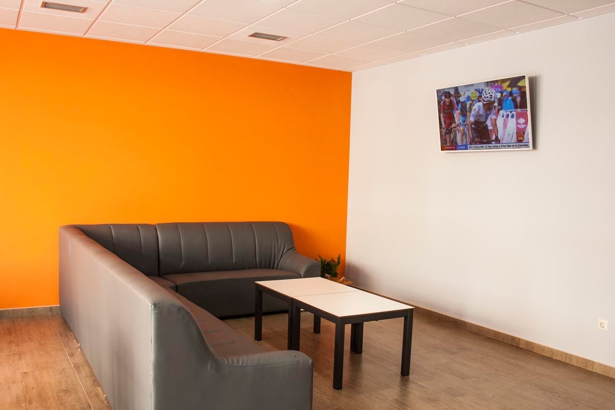 Una sala de espera moderna con un sofá seccional gris, una pared naranja, una mesa pequeña y un cuadro enmarcado.
