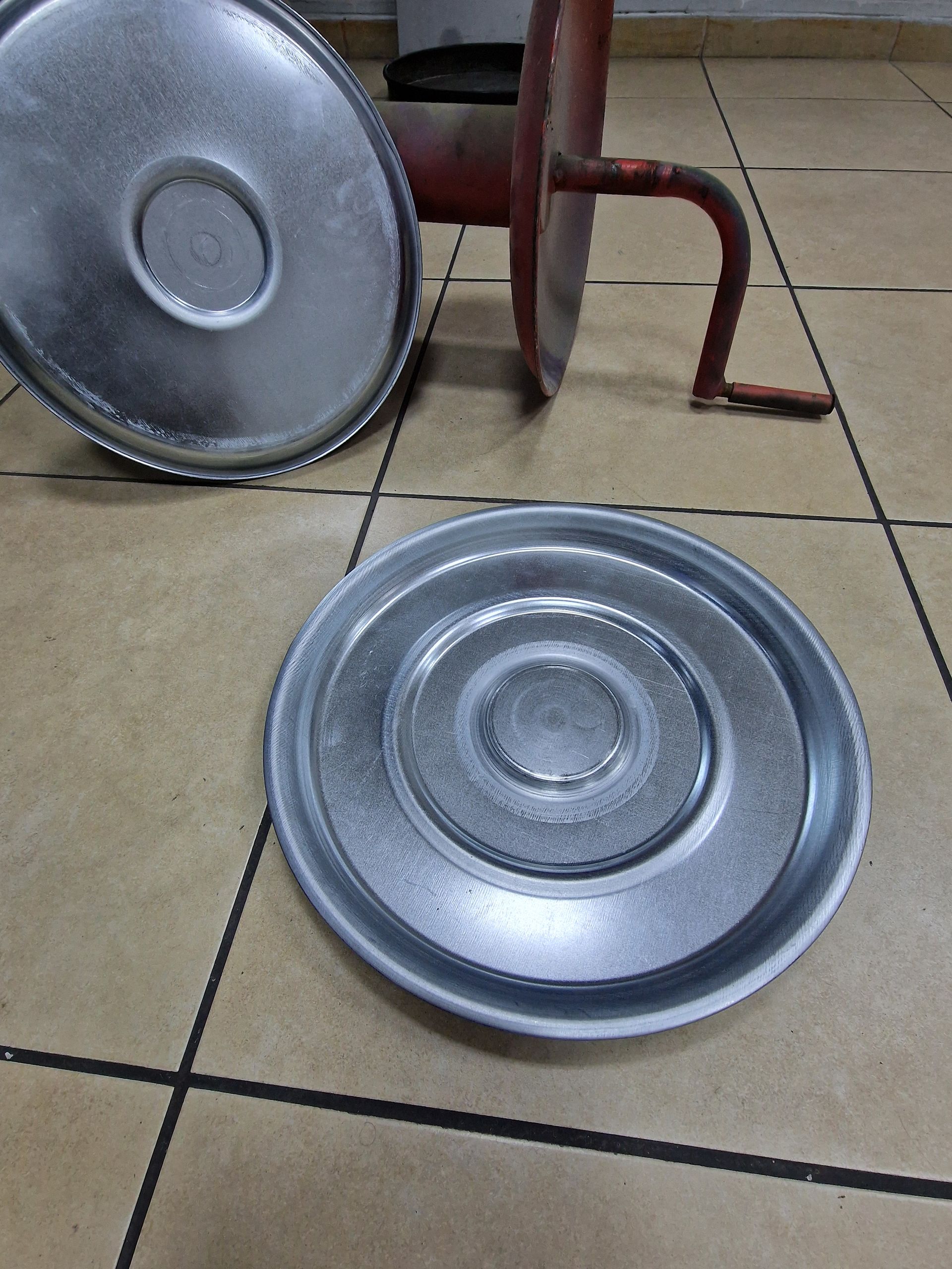 Αποσυναρμολογημένη μεταλλική συσκευή κουζίνας, πιθανώς ένας μύλος, σε πλακάκια δαπέδου.