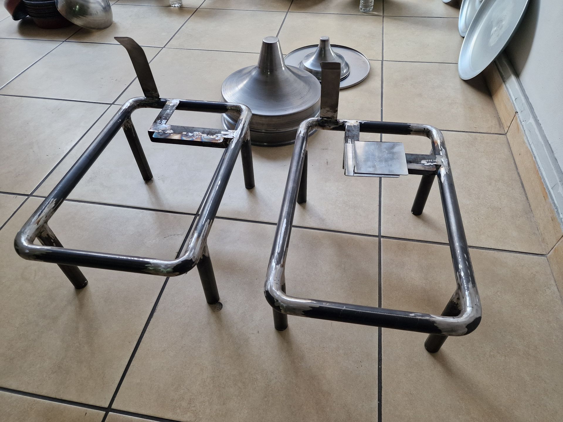 Δύο συγκολλημένα μεταλλικά πλαίσια, με μεταλλικές χοάνες και πλάκες, βρίσκονται πάνω σε ένα πλακάκι δαπέδου.