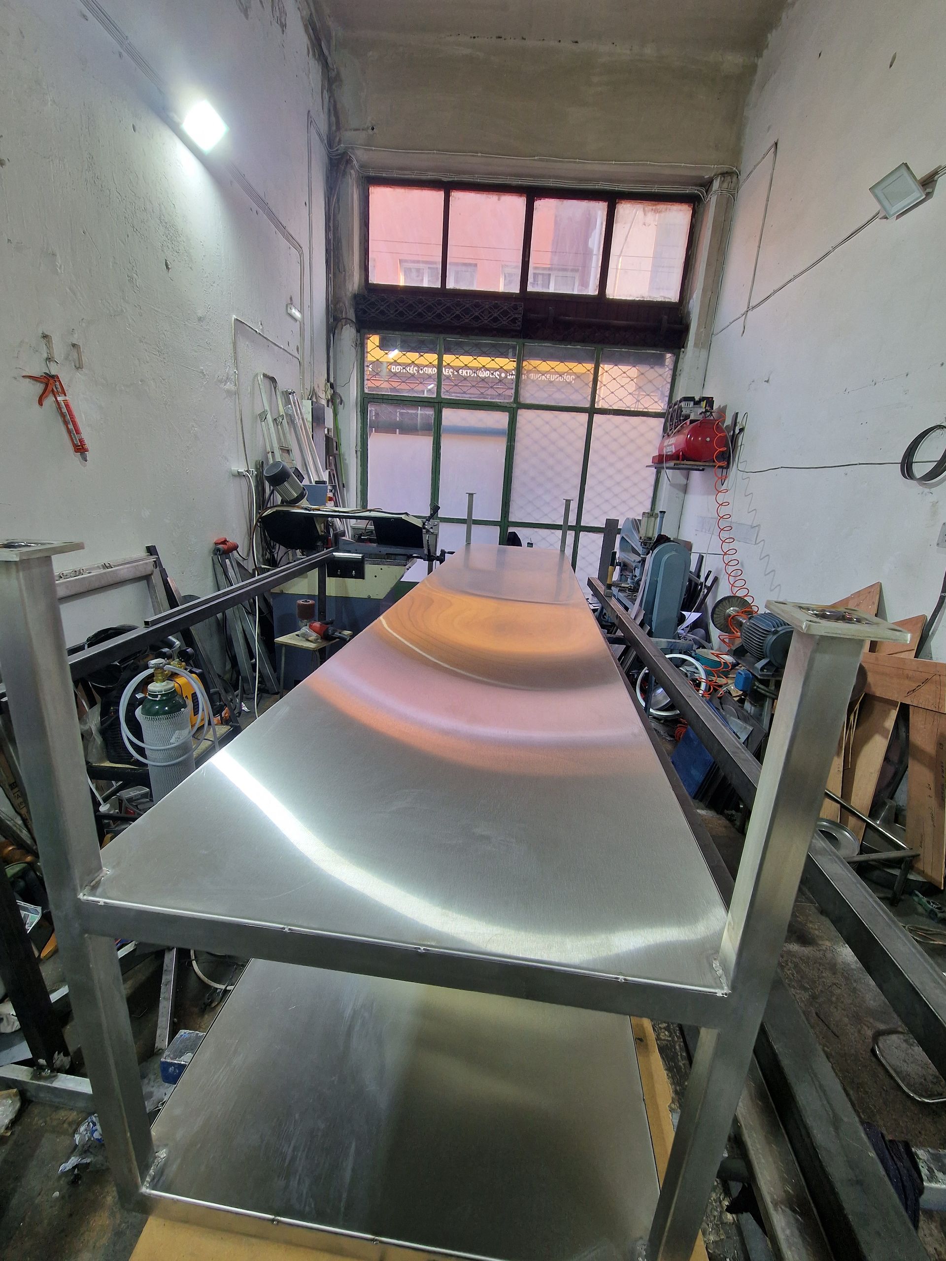 Μακρύ τραπέζι εργασίας από ανοξείδωτο ατσάλι σε περιβάλλον εργαστηρίου.