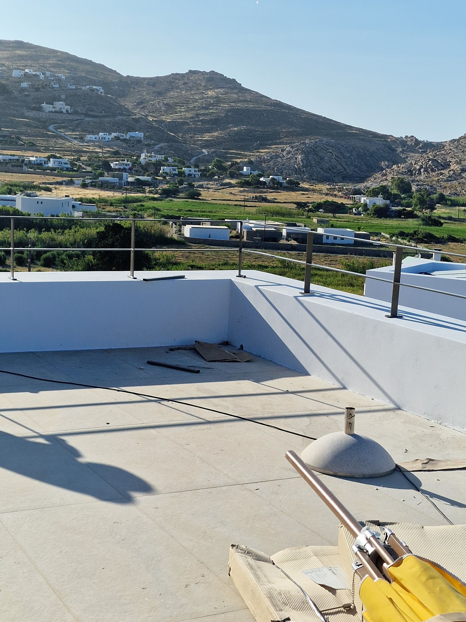 Θέα από την ταράτσα μιας κοιλάδας και βουνών. Διακρίνονται τσιμεντένιοι τοίχοι, μεταλλικοί στύλοι και μια μερική θολωτή κατασκευή.