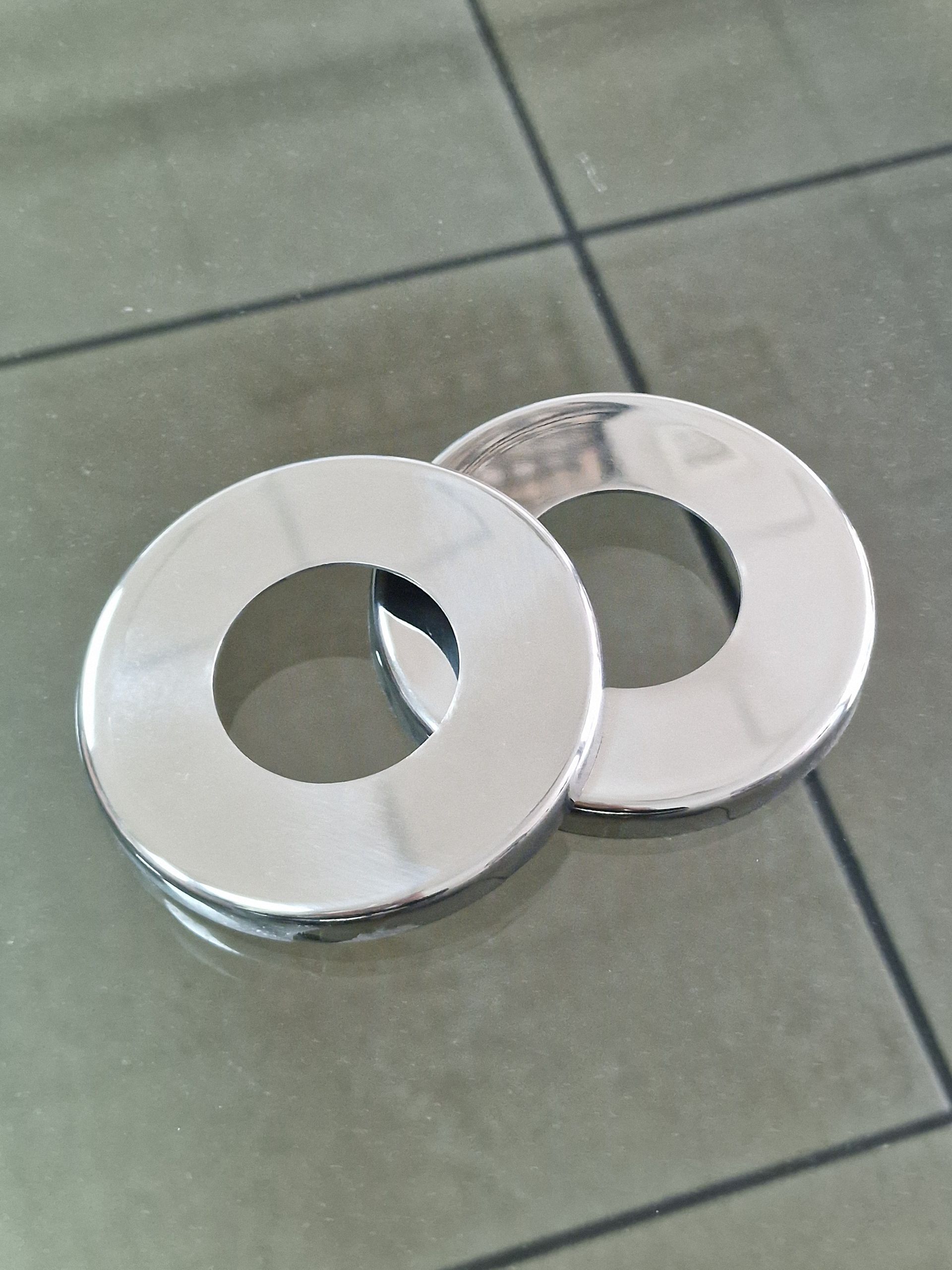 Δύο γυαλιστερά, στρογγυλά, μεταλλικά θυρείδια σωλήνων σε πλακάκια.