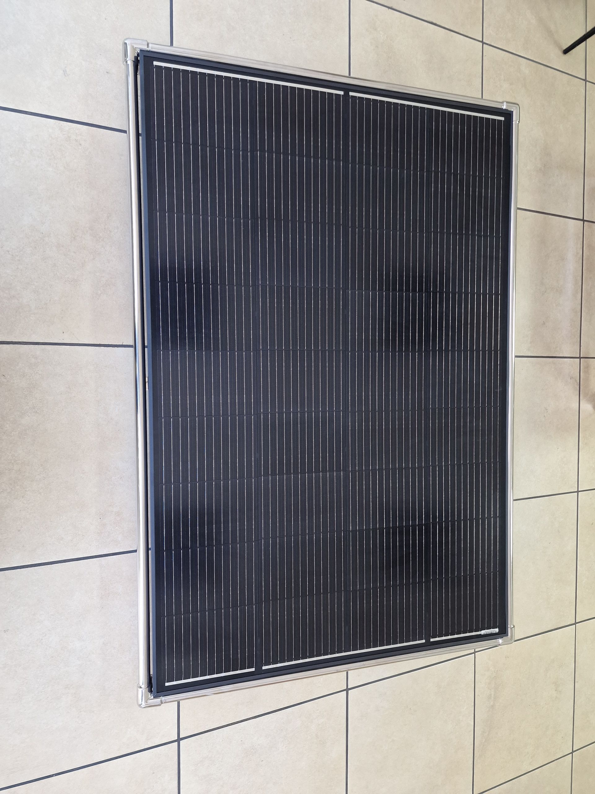 Μαύρο ηλιακό πάνελ με μεταλλικό πλαίσιο σε πλακάκι δαπέδου.
