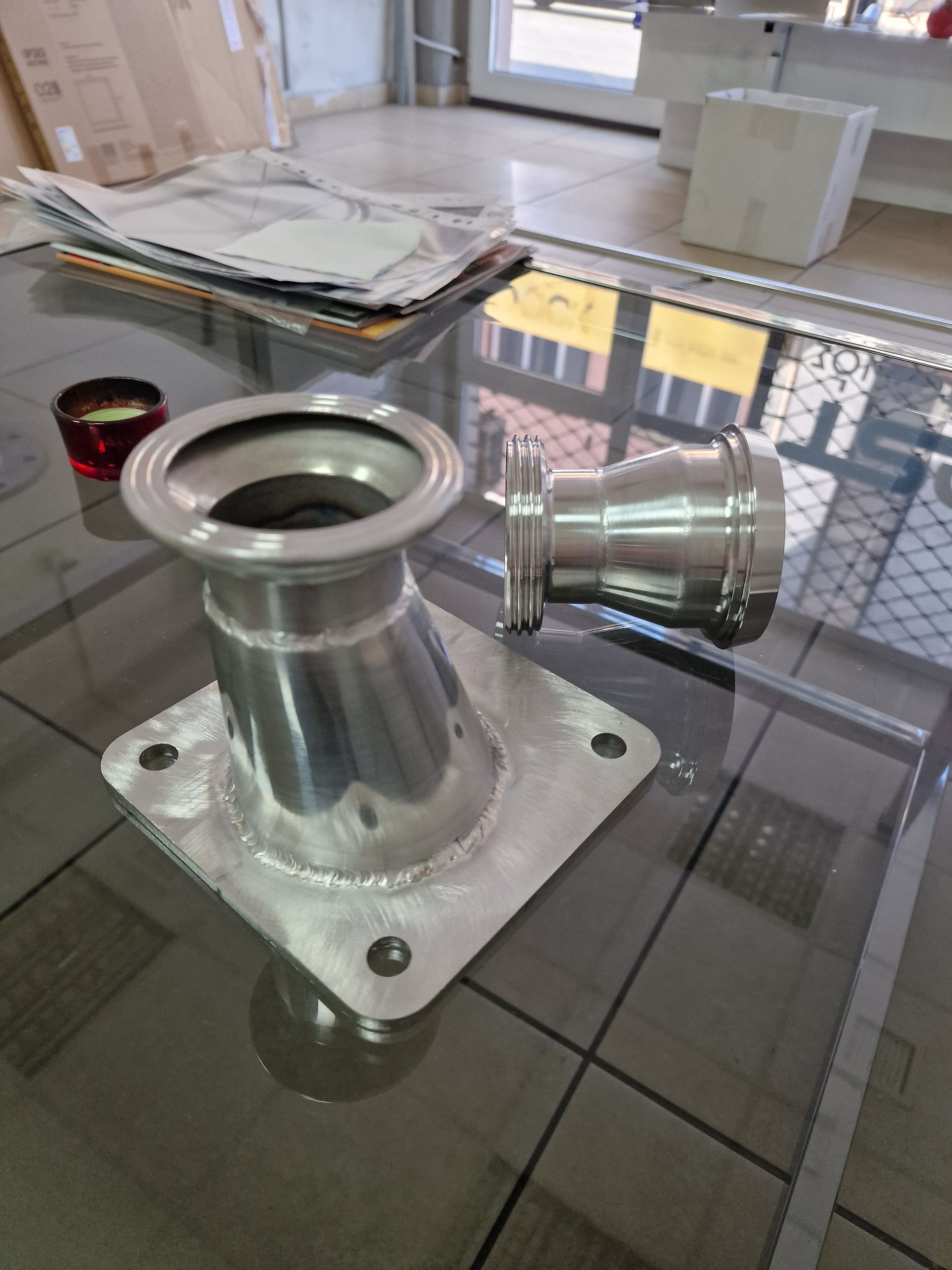 Βιομηχανικά εξαρτήματα σωλήνων από ανοξείδωτο χάλυβα σε γυάλινο τραπέζι.