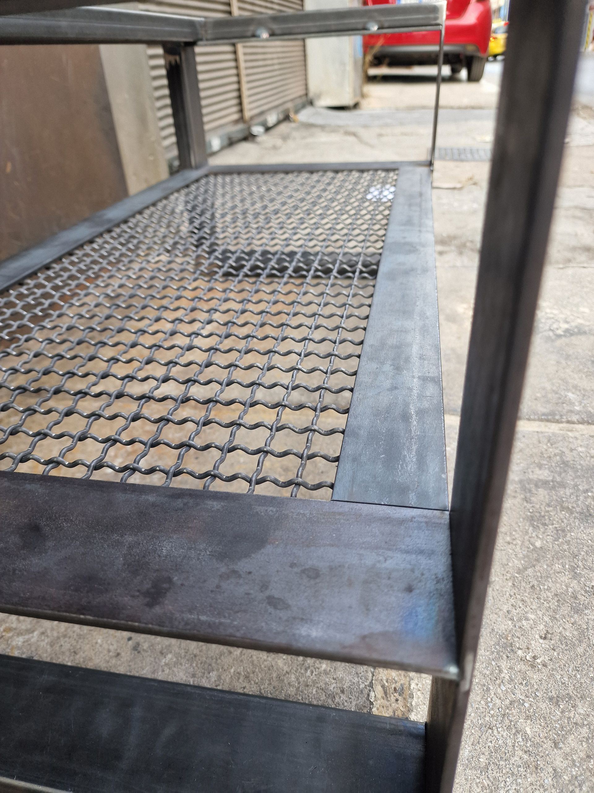 Ράφι από μεταλλικό πλέγμα με συρματόπλεγμα· κοντινό πλάνο δείχνει τη γωνία βιομηχανικής μονάδας ραφιών, σε εξωτερικό χώρο.