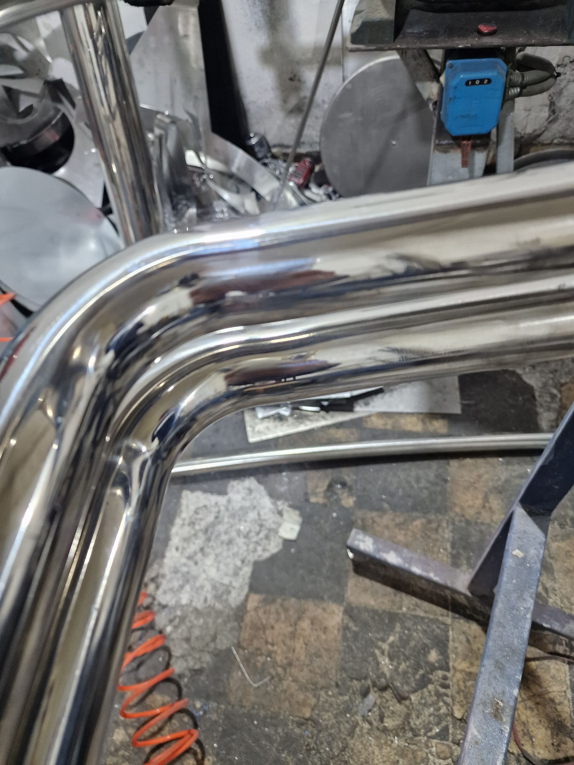 Λαμπερός μεταλλικός σωλήνας λυγισμένος σε ορθή γωνία. Βιομηχανικό εργαστήριο με εξοπλισμό συγκόλλησης στο φόντο.