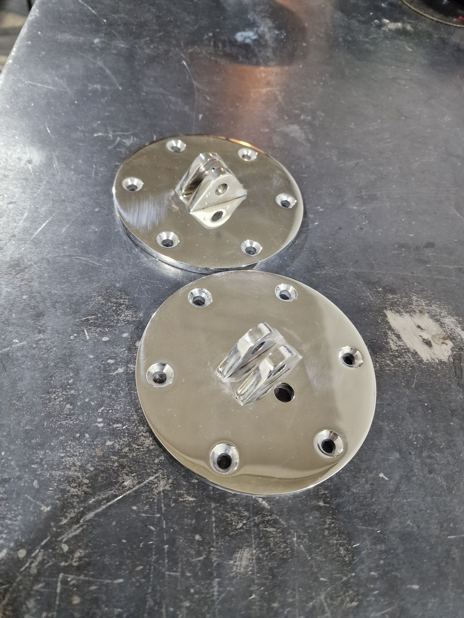 Δύο κυκλικά μεταλλικά κομμάτια με υπερυψωμένα κεντρικά τμήματα και πολλαπλές τρύπες, σε ανάγλυφη επιφάνεια.