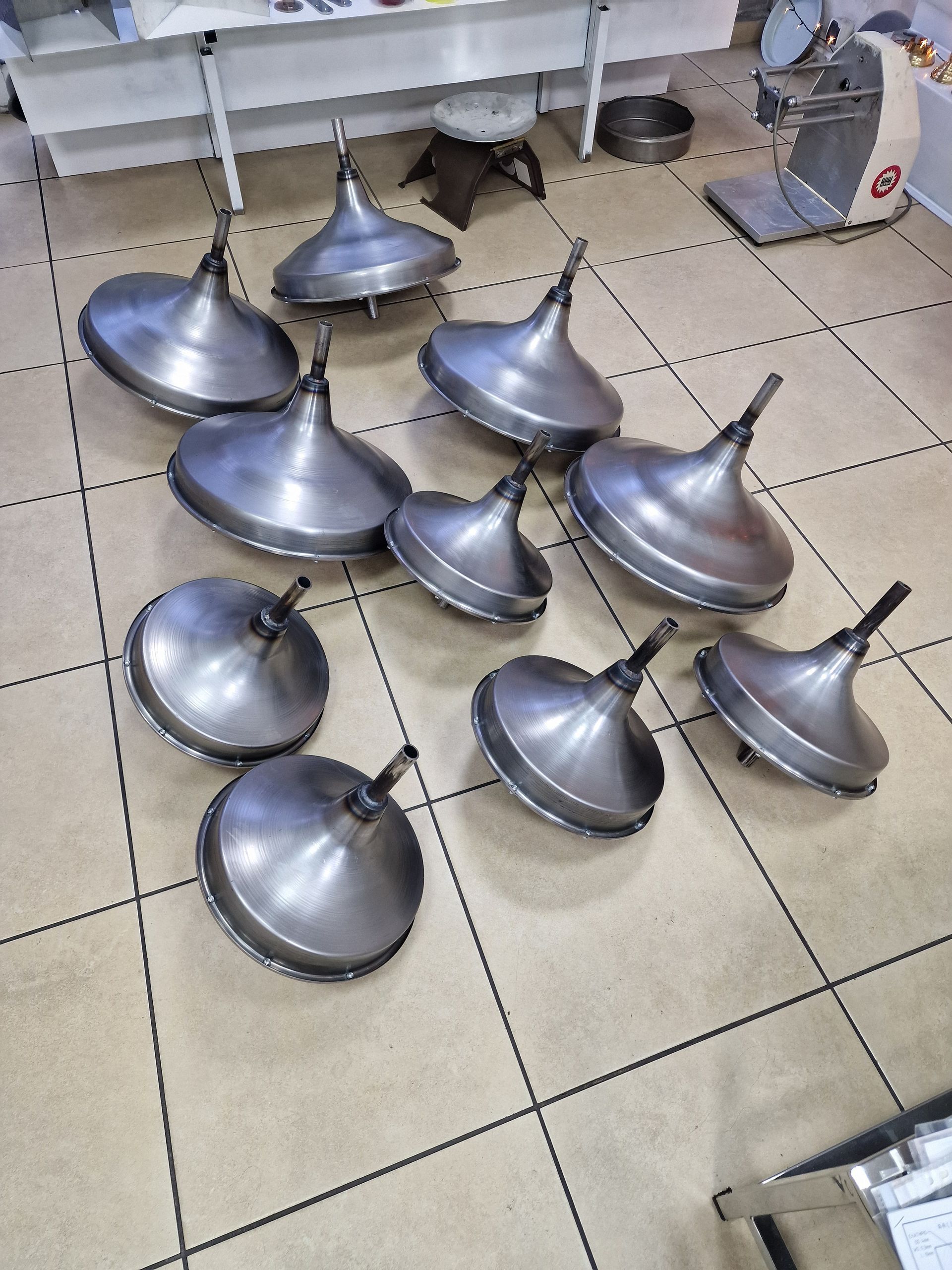 Δέκα αναποδογυρισμένα μεταλλικά κωνικά σχήματα με μίσχους, διάσπαρτα σε πλακάκια δαπέδου.