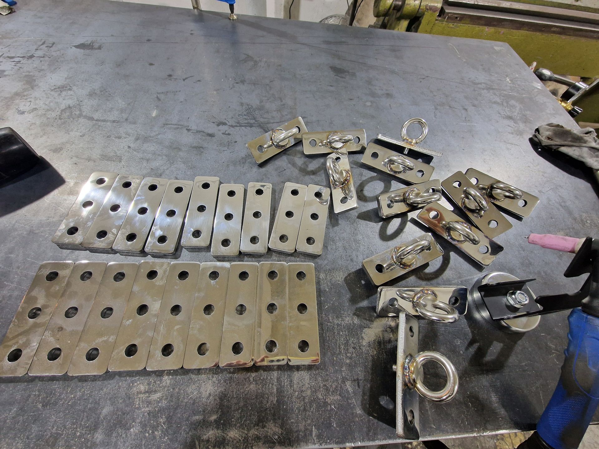 Μεταλλικά κομμάτια με τρύπες και συγκολλημένους δακτυλίους σε μεταλλικό τραπέζι σε εργαστήριο.