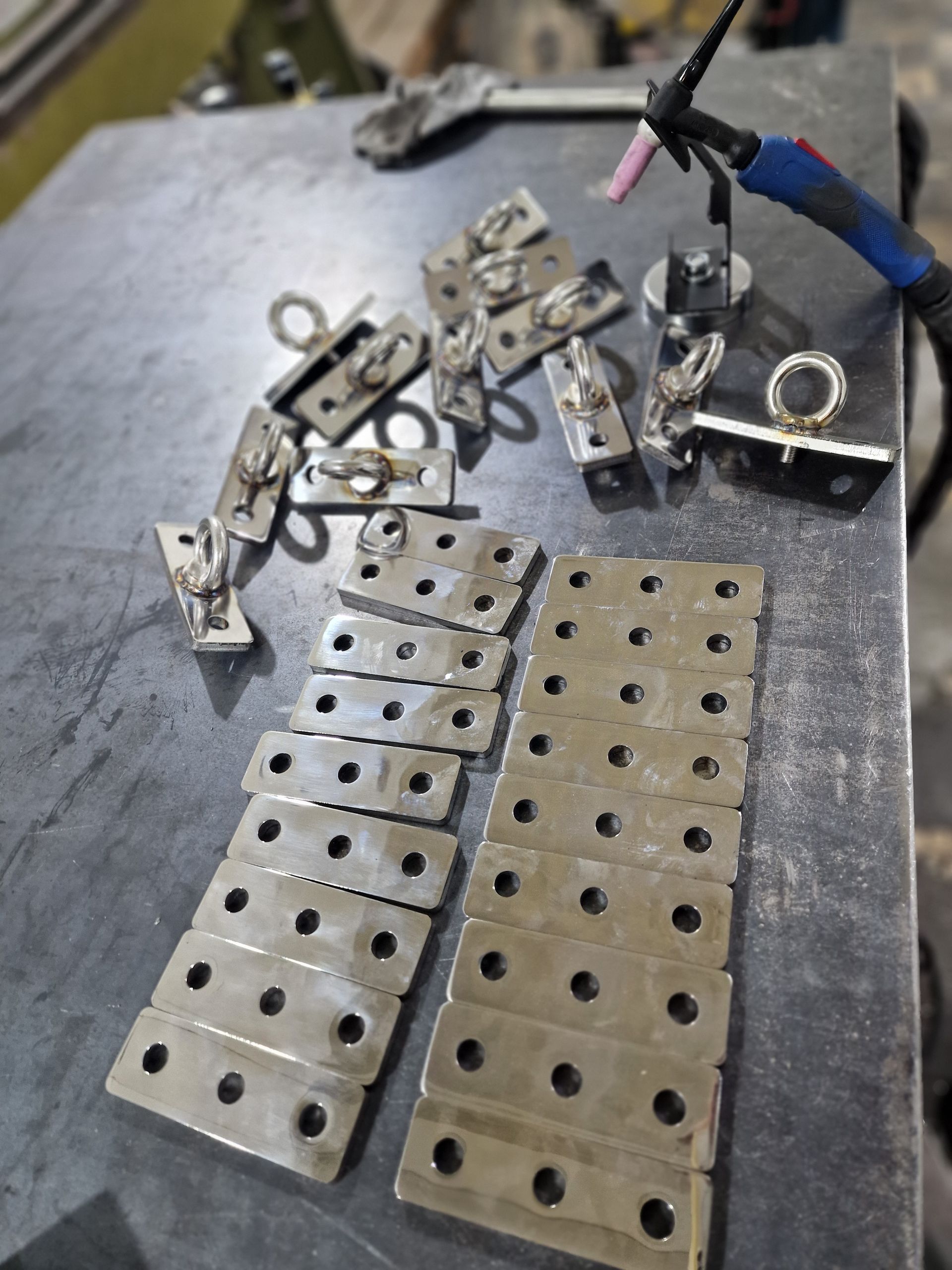 Μεταλλικές πλάκες με οπές και συγκολλημένους δακτυλίους, διατεταγμένες σε μεταλλική επιφάνεια κοντά σε πυρσό συγκόλλησης.