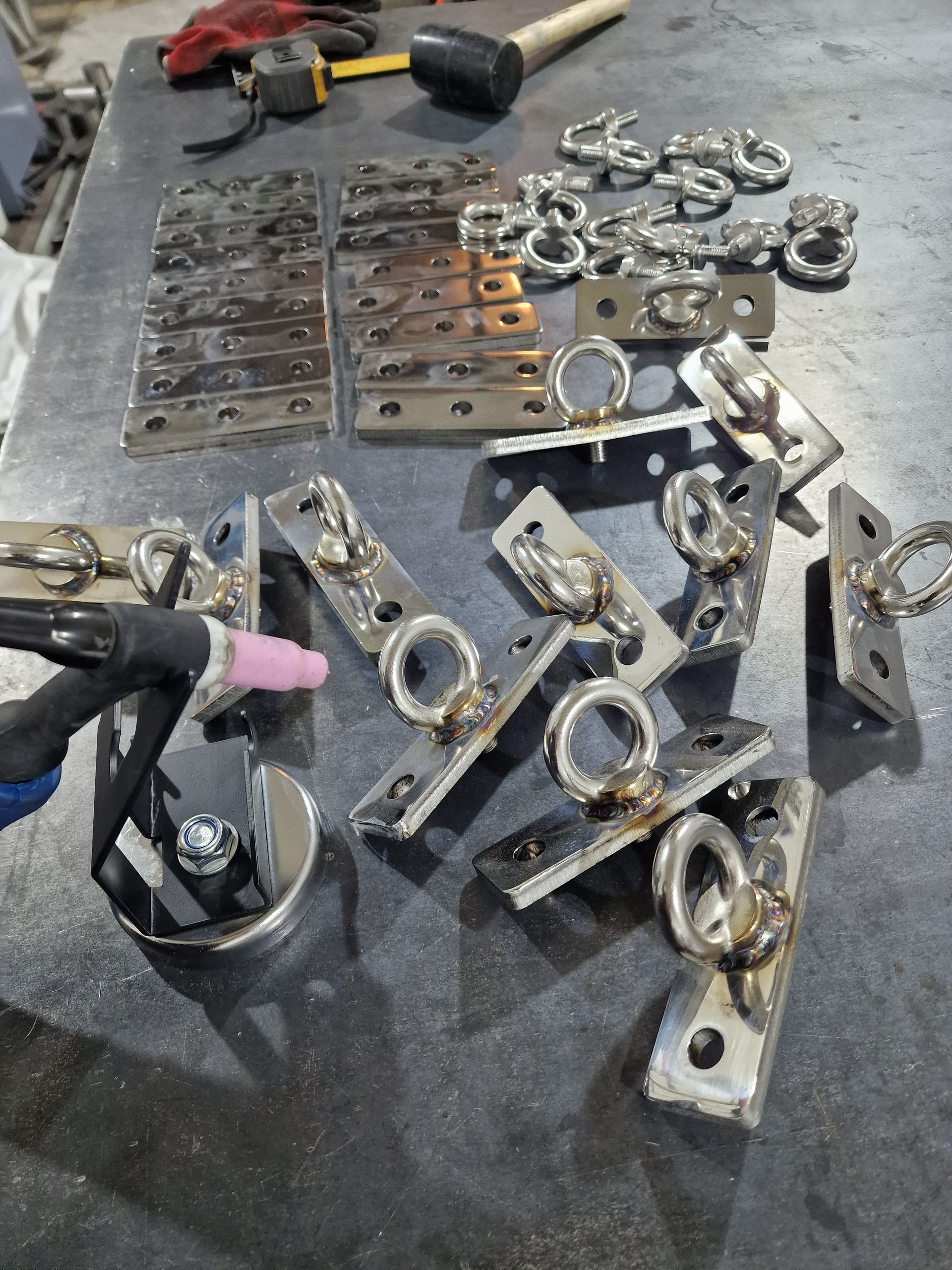 Συγκολλητής που συναρμολογεί μεταλλικά στηρίγματα με δακτυλίους, εργαλεία σε πάγκο εργασίας.