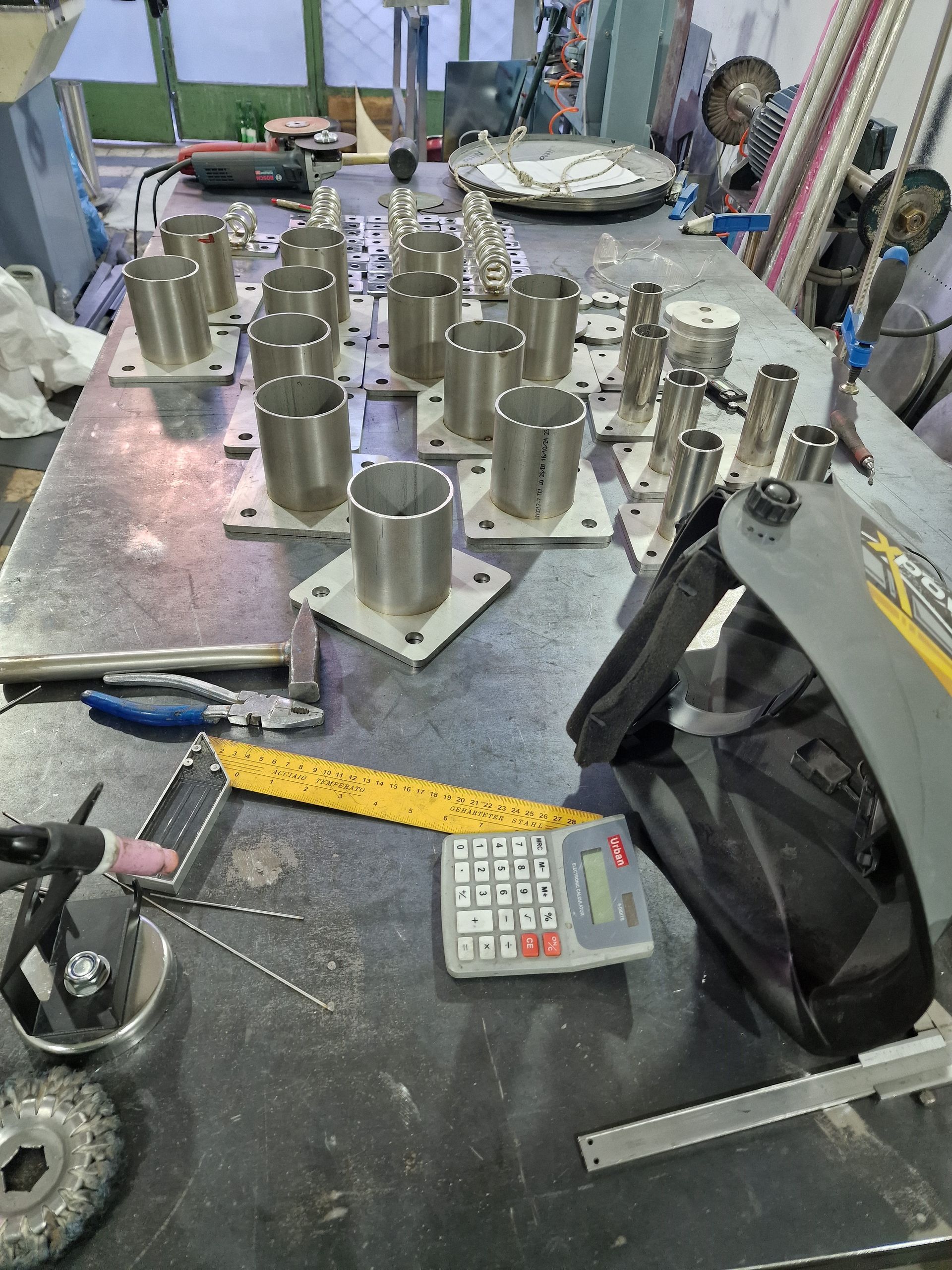 Χώρος εργασίας μεταλλικών κατασκευών με κυλινδρικά μεταλλικά μέρη διατεταγμένα σε τραπέζι με εργαλεία.