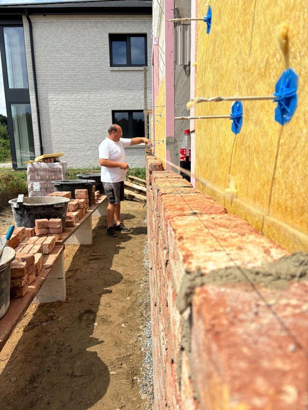 Ein Mann errichtet auf einer Baustelle eine Ziegelmauer neben einer gelben, isolierten Wand.