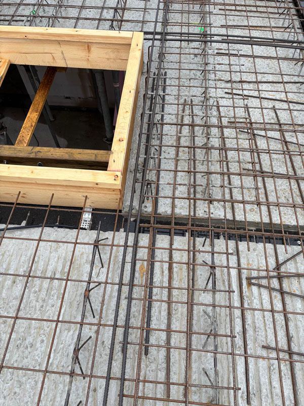 Bewehrungsstahlstäbe liegen auf einer Betonplatte in der Nähe eines hölzernen Fensterrahmens und sind bereit zum Betonieren.