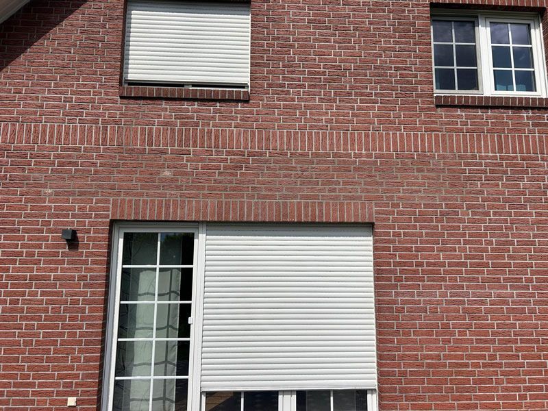 Rotes Backsteingebäude mit geschlossenen weißen Fensterläden und Fenstern.