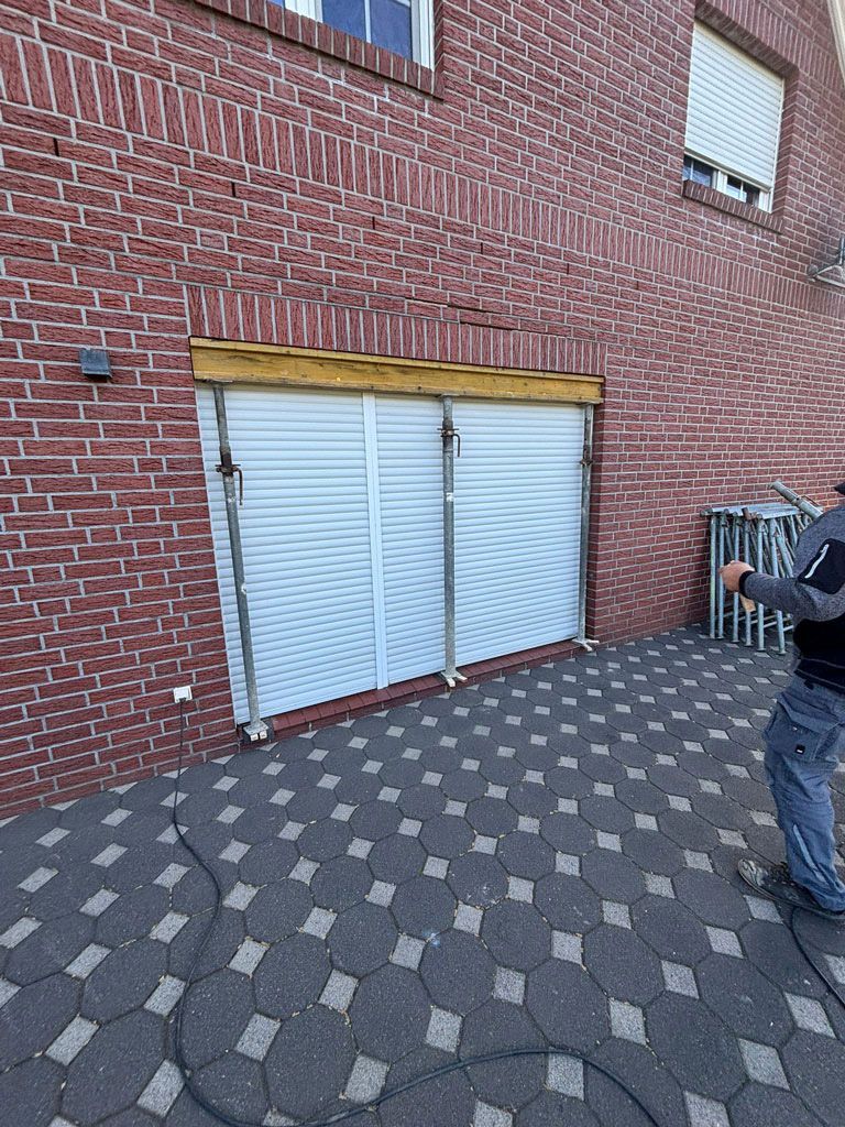 Gebäudeaußenansicht mit Backsteinmauer, geschlossenen weißen Jalousien und einer Person mit Klemmbrett.