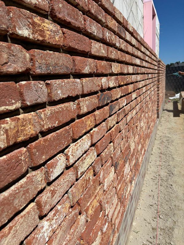 Im Bau befindliche rote Backsteinmauer, teilweise an ein rosafarbenes Gebäude angebaut, im Freien.