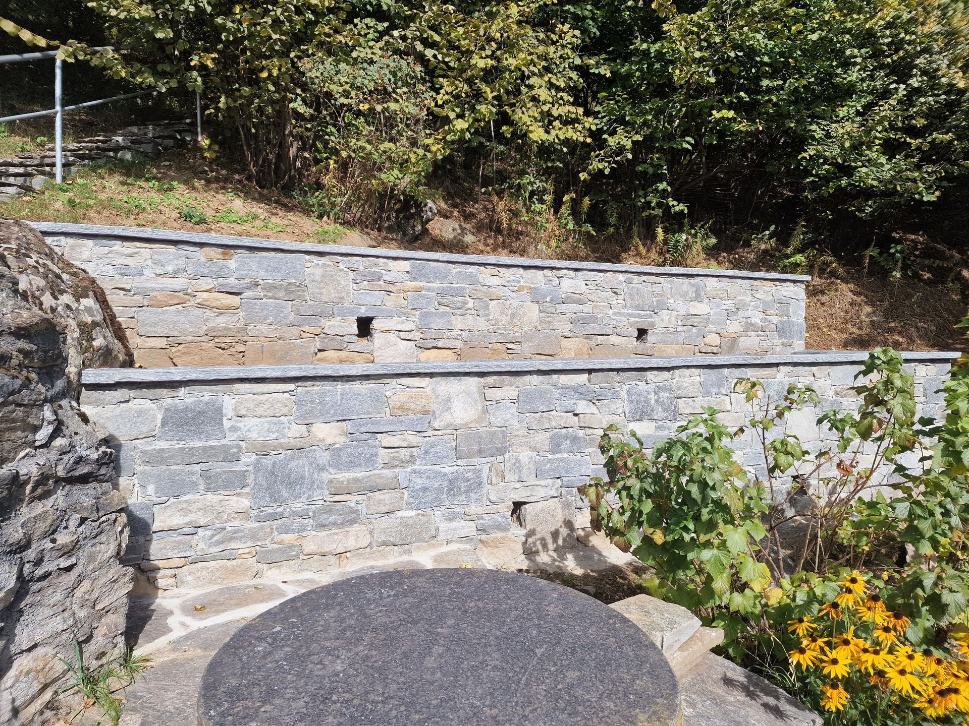 Muri di contenimento in pietra in un giardino in collina, con scale e vegetazione.