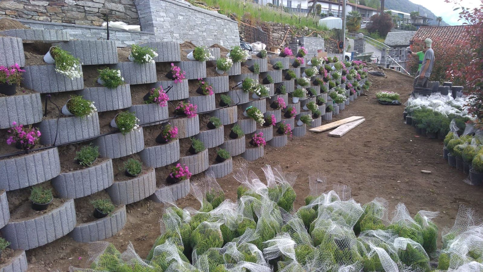 Muro di contenimento grigio con fiori in vaso e giardino paesaggistico.