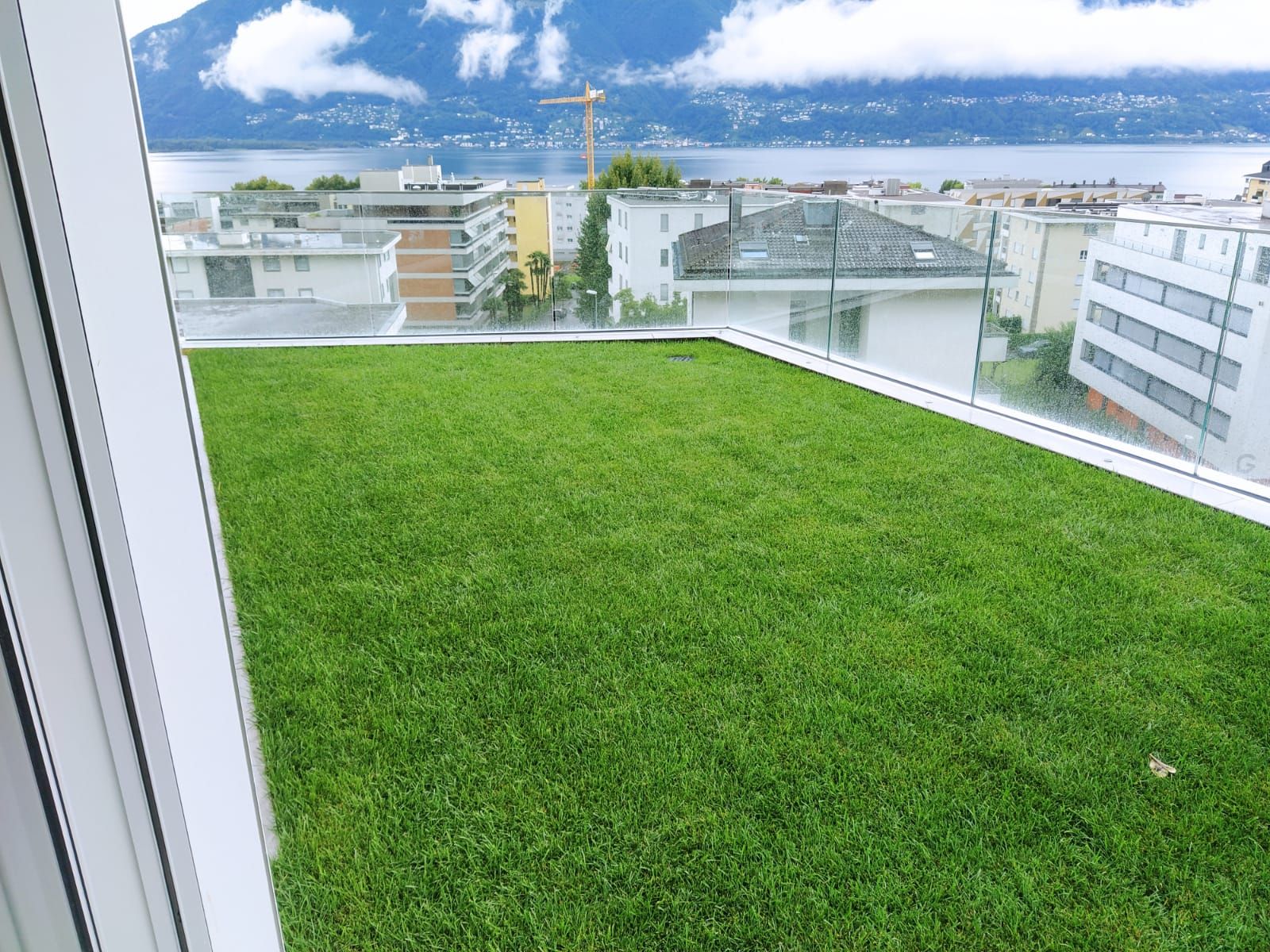 Prato verde sul tetto con vista sulla città e sul lago, incorniciato da bianco e vetro.