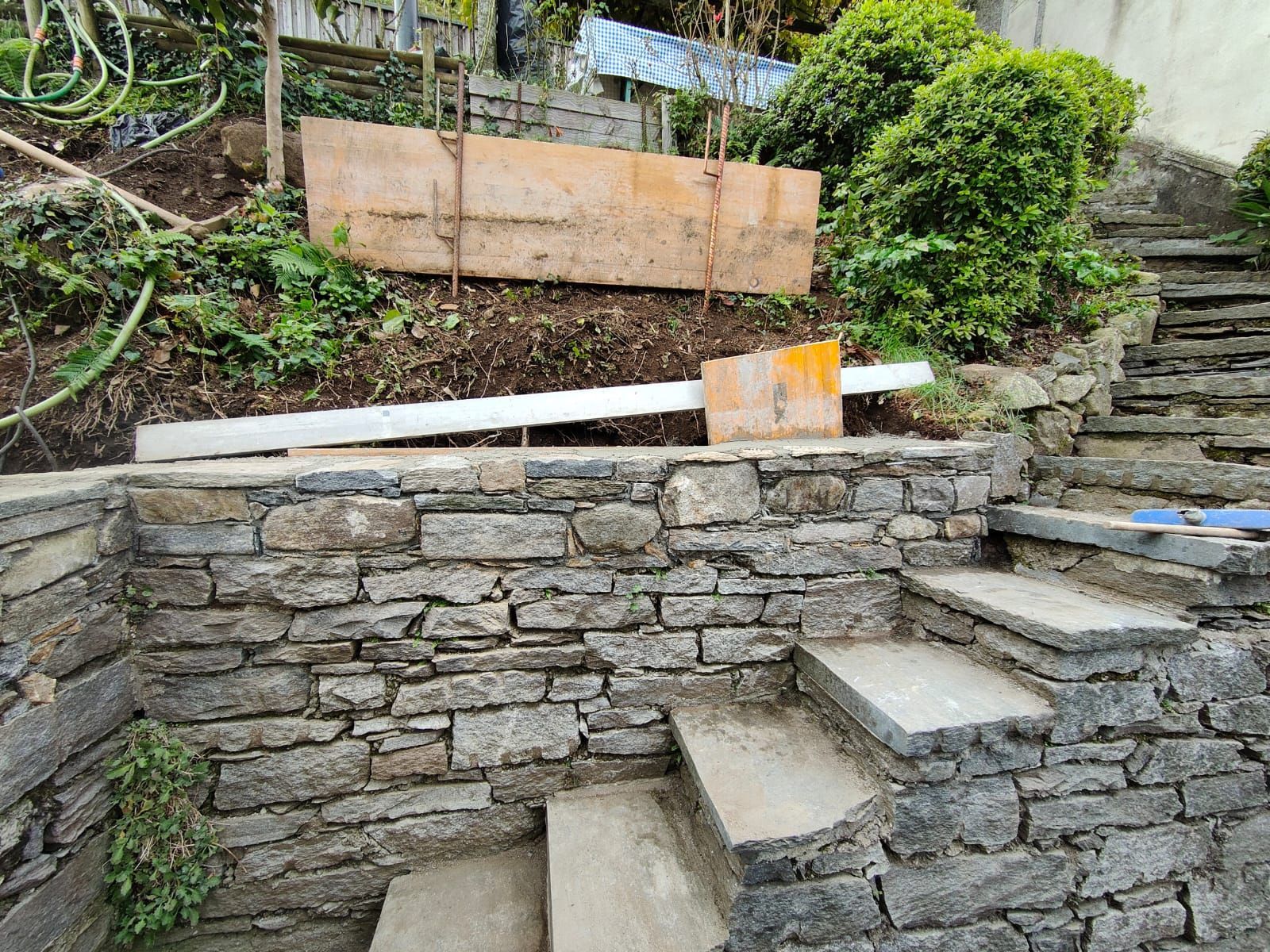 Scala in pietra e muro di contenimento in un giardino, con assi di legno sopra.