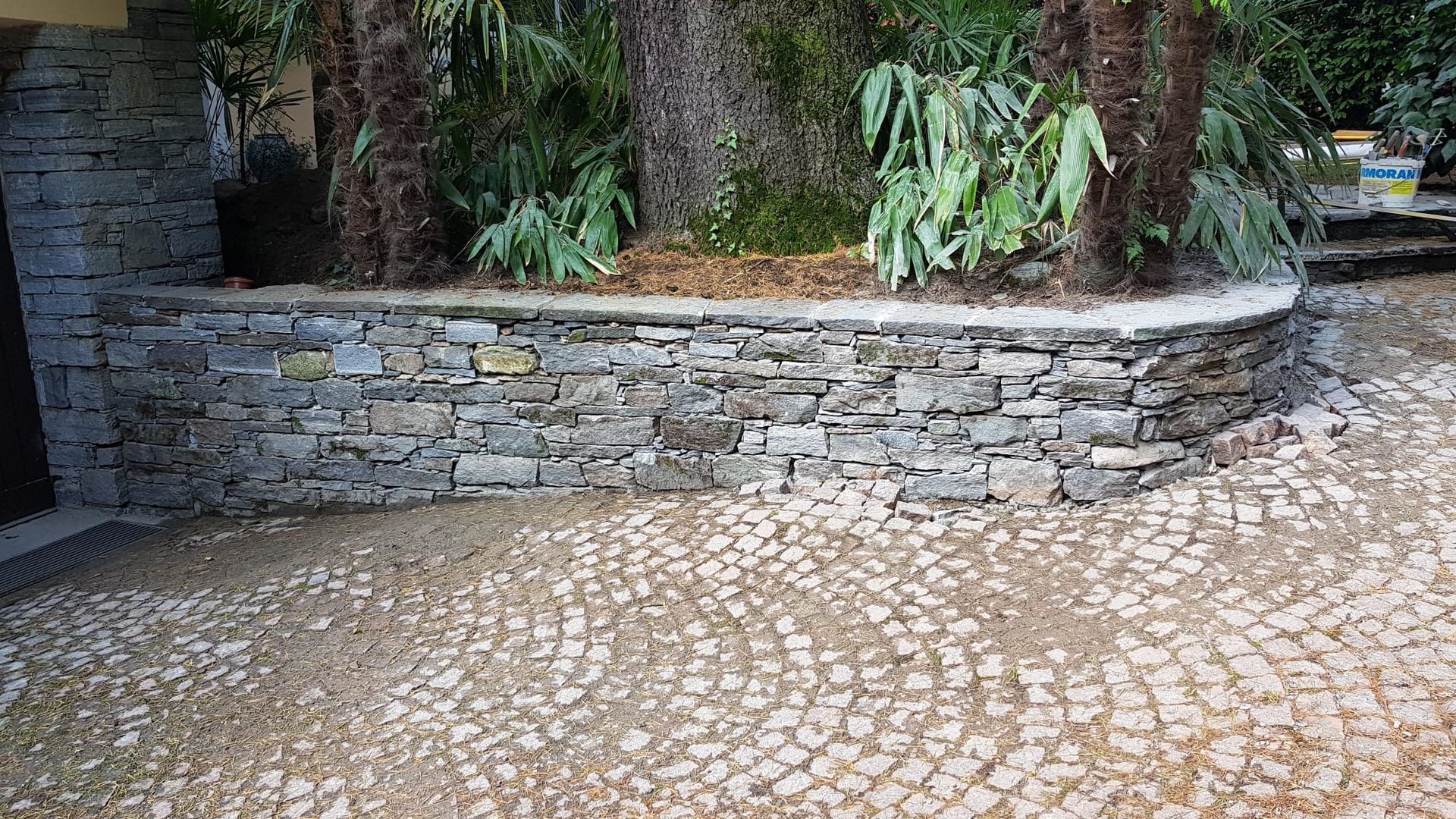 Muro in pietra con piante in vaso lungo un cortile lastricato.