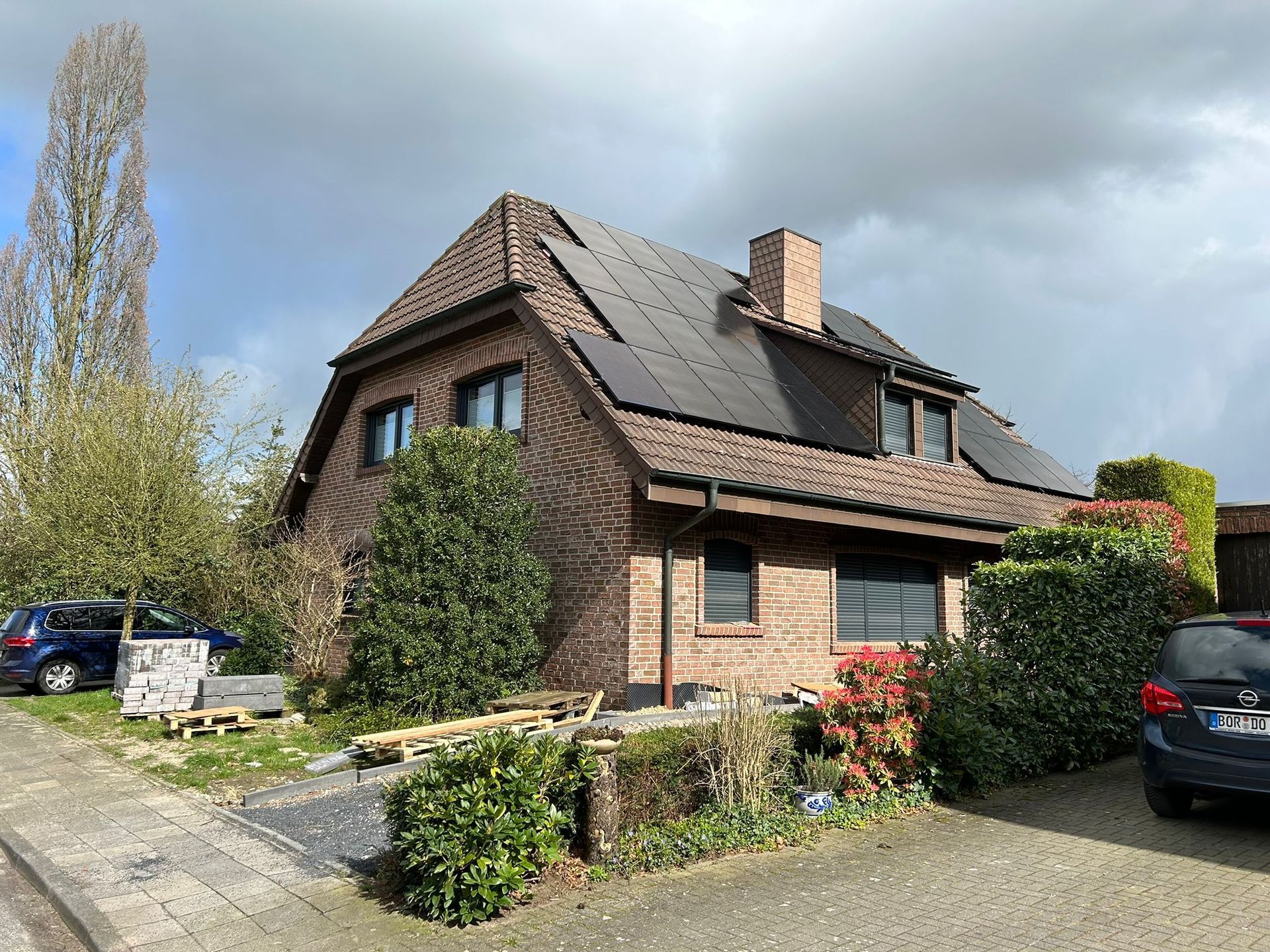 Ein Backsteinhaus mit Solarzellen auf dem Dach und einem davor geparkten Auto.