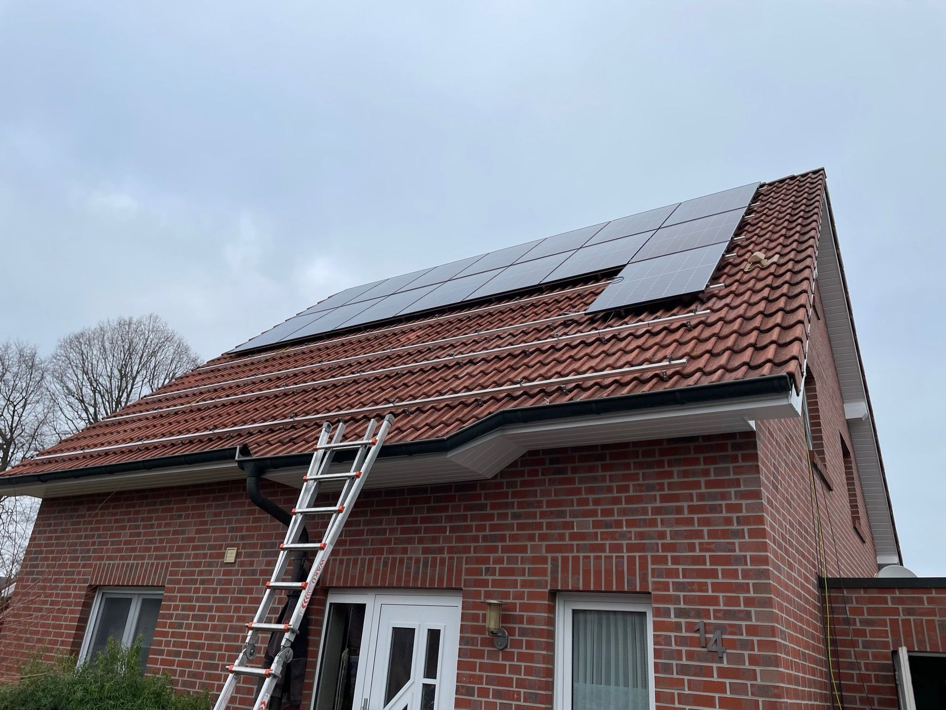 Auf einem Backsteinhaus mit Solarzellen auf dem Dach steht eine Leiter.