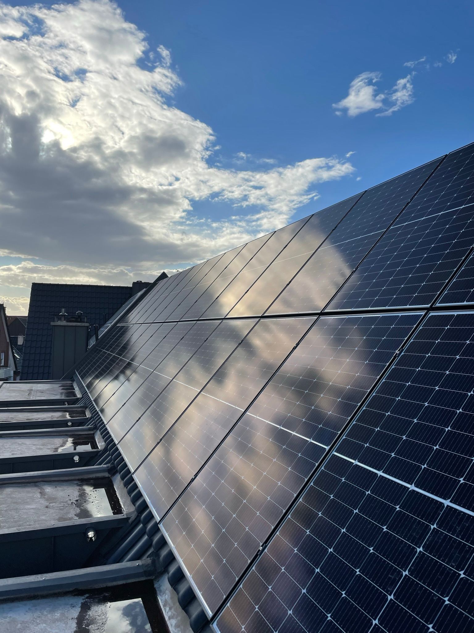 Eine Reihe von Solarmodulen auf einem Dach mit einem blauen Himmel im Hintergrund.